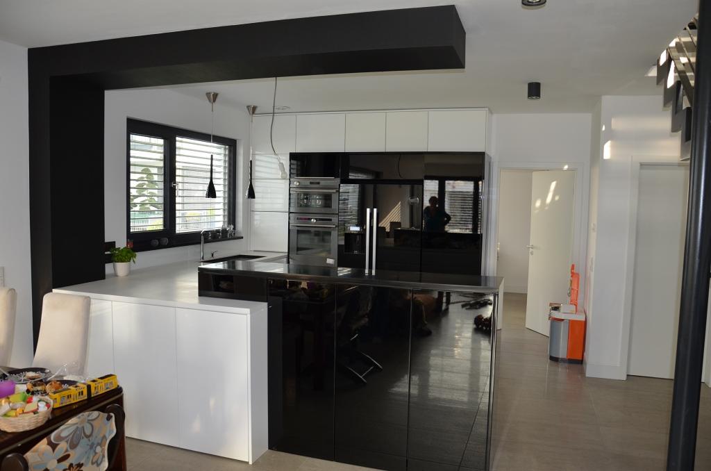 Nowoczesna kuchnia z wyspą w czarno-białej kolorystyce, z czarnymi, wiszącymi lampami i dużym oknem z żaluzjami.