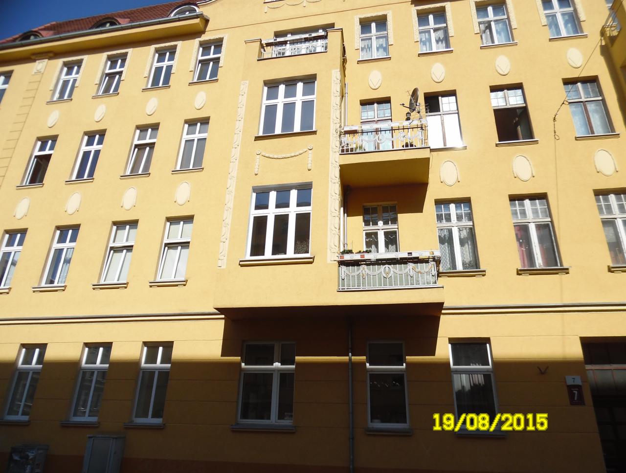 Elewacja kamienicy w odcieniach żółci z balkonami i białymi oknami, widok z dołu w słoneczny dzień.