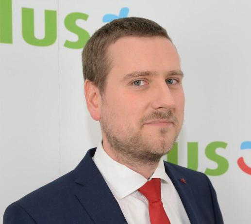 Portret mężczyzny w garniturze i czerwonym krawacie na tle logotypu telekomunikacyjnego operatora.