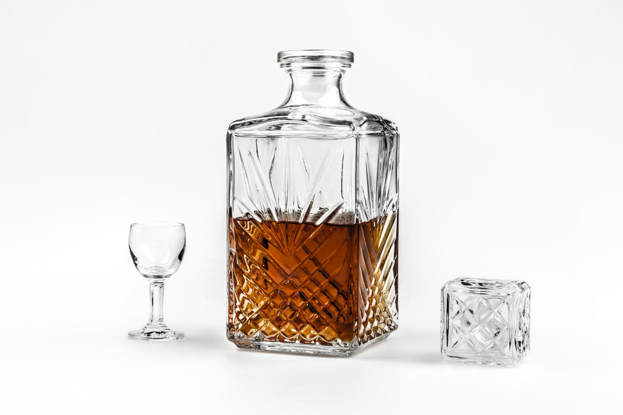 Kryształowa karafka z bursztynowym trunkiem, kieliszek do wódki i kwadratowy korek na białym tle, prezentacja produktu.