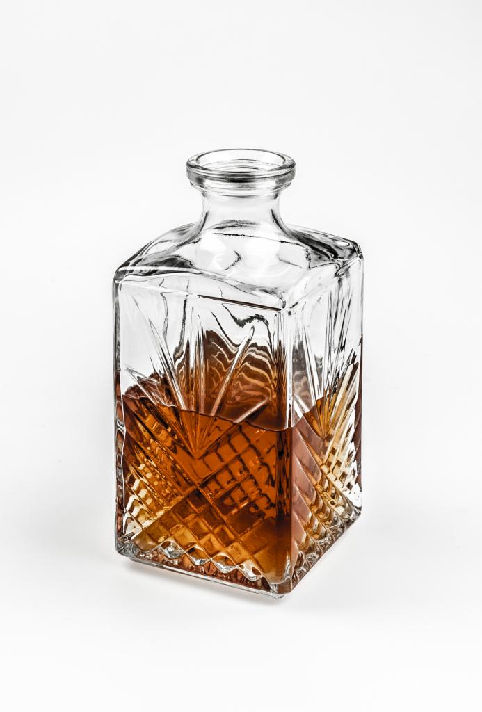 Kwadratowa, szklana karafka z geometrycznym wzorem wypełniona bursztynowym płynem na białym tle.