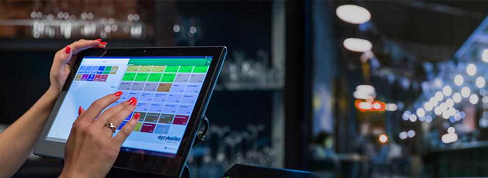 Kobieta z czerwonym manicure dotyka ekranu dotykowego tabletu z oprogramowaniem POS w lokalu gastronomicznym, widoczne logo 'dotykacko'