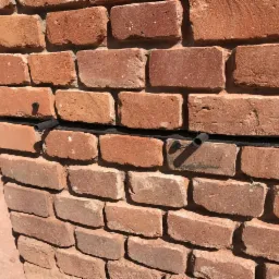 Czerwona ściana z cegieł z zainstalowanym systemem osuszania: czarny przewód z rurkami w otworach między cegłami.