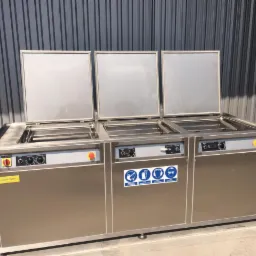 Profesjonalna, przemysłowa myjka ultradźwiękowa ze stali nierdzewnej z trzema komorami, każda z uchylną pokrywą, panele sterowania z pokrętłami i przyciskami, naklejki informacyjne na froncie,...