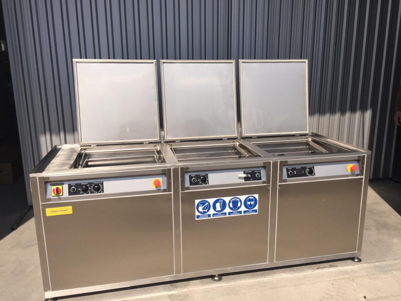 Profesjonalna, przemysłowa myjka ultradźwiękowa ze stali nierdzewnej z trzema komorami, każda z uchylną pokrywą, panele sterowania z pokrętłami i przyciskami, naklejki informacyjne na froncie,...