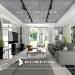 Salon w szarościach z marmurową podłogą, szary narożnik z narzutą, biały regał z książkami, betonowy sufit z reflektorami i logo firmy Biuromax w dolnej części zdjęcia.