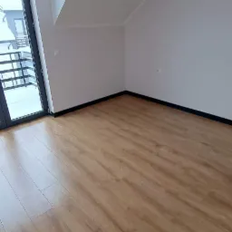 Jasne panele podłogowe ułożone w nowym pokoju z oknem balkonowym i skośnym sufitem.