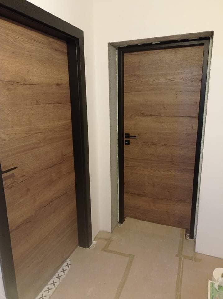 Dwa skrzydła drzwi wewnętrznych z okleiną drewnopodobną i czarnymi ościeżnicami, widoczne w trakcie montażu w Myślenicach, z detalami wykończenia podłogi.