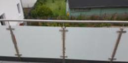 Szklana balustrada balkonu z nierdzewnymi elementami mocującymi i widokiem na zieleń w tle.