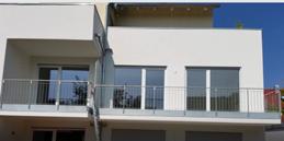 Nowoczesny budynek z balkonami zabezpieczonymi metalowymi balustradami, widok z zewnątrz, okna z roletami zewnętrznymi.