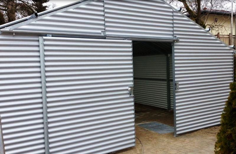 Metalowa konstrukcja z falistej blachy z częściowo otwartymi przesuwnymi drzwiami, widoczne mocowania szyn i zamek.