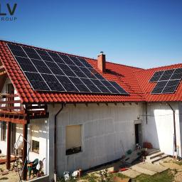 SELV GROUP - FOTOWOLTAIKA, POMPY CIEPŁA, KLIMATYZACJE - Dom jednorodzinny z czerwoną dachówką, na której zamontowano panele słoneczne; widoczny fragment ogrodu z narzędziami i materiałami budowlanymi.