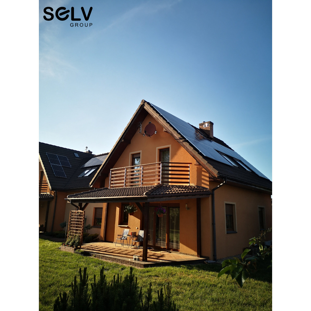 Dom jednorodzinny z panelami słonecznymi na dachu, widok z ogrodu, logo firmy w lewym górnym rogu.