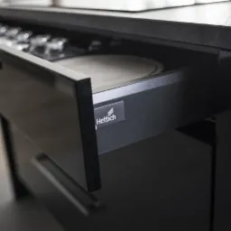 Otwarta szuflada kuchenna w czarnym, matowym wykończeniu z widocznym systemem organizacji wewnętrznej i logo Hettich na froncie.