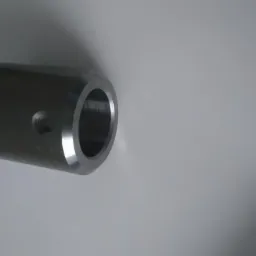 Metalowy cylinder z dwoma gwintowanymi otworami bocznymi, leżący na białym tle.