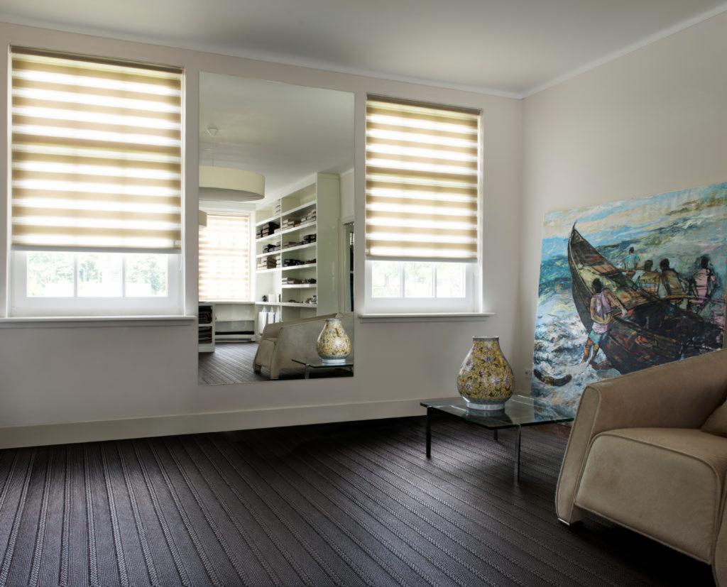 Nowoczesne okno z beżowo-białymi osłonami okiennymi, odbicie wnętrza garderoby w lustrze, obraz z motywem morskim, stylowy fotel i ciemna podłoga.