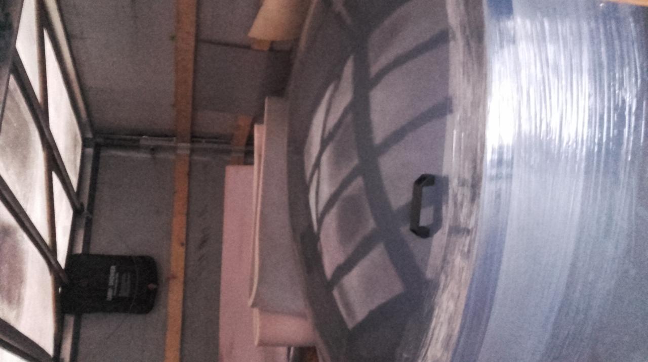 Duży, okrągły przedmiot owinięty folią stretch z czarnym uchwytem, znajdujący się wewnątrz pojazdu dostawczego z widoczną konstrukcją ramy i oświetleniem.