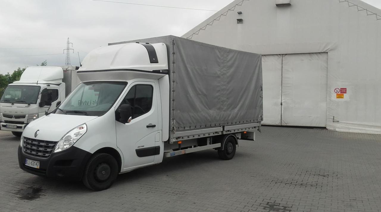 Dwa białe busy transportowe na tle magazynu z metalowymi drzwiami, jeden z plandeką, drugi bez.