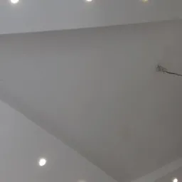 Biały sufit z wbudowanymi punktowymi lampami LED, widoczne przewody elektryczne przy jednej z lamp, ukośne łączenie powierzchni sufitu