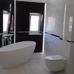 Nowoczesna łazienka z wolnostojącą wanną, podwieszaną toaletą i czarno-białymi płytkami z oświetleniem LED.