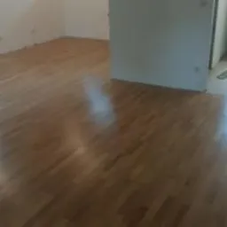 Wykończona podłoga z jasnego drewna w pustym pomieszczeniu, widoczne ślady po szpachlowaniu na ścianach, przygotowane do dalszych prac wykończeniowych.