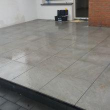 Wykończony taras z szarych, matowych płytek gresowych ułożonych na zewnątrz, widoczna skrzynka narzędziowa w tle.