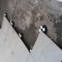 Układanie płytek podłogowych z użyciem systemów poziomowania, widoczne czarne klipsy i białe kliny, surowy stan posadzki przed fugowaniem.