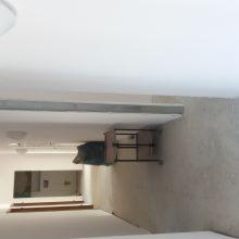 Wnętrze w trakcie prac wykończeniowych: surowa ściana, widoczny stół roboczy, przygotowane podłoże pod malowanie lub położenie tapety.