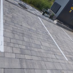 STAN-BRUK - Szara kostka brukowa z białymi liniami wyznaczającymi miejsca parkingowe, widok z góry, obok transformator i trawa.