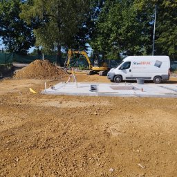 STAN-BRUK - Przygotowany teren pod fundamenty z widocznym zbrojeniem, niwelatorem, koparką i samochodem dostawczym firmy StanBRUK w słoneczny dzień.