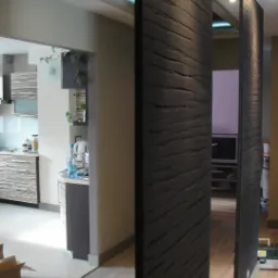 Dekoracyjne, czarne panele działowe z wyraźną fakturą drewna oddzielają przestrzeń w nowoczesnym wnętrzu. W tle widoczna kuchnia i salon z oświetleniem sufitowym.