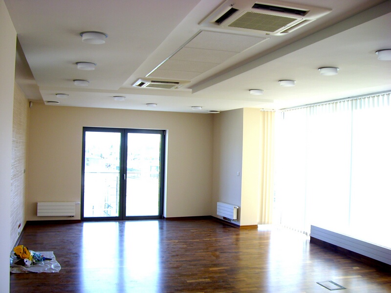 Wnętrze biura po remoncie: parkiet, ściany w odcieniach beżu, duże okna z pionowymi żaluzjami, podwieszany sufit z klimatyzacją, grzejniki pod oknami.