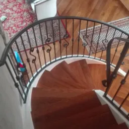 Spiralne, drewniane schody z czarną, kutą balustradą w domu w Trzciance, widziane z góry, z elementami wystroju wnętrza w tle.