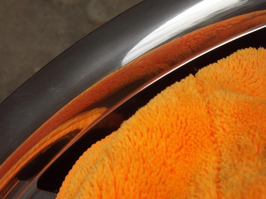 Fragment polerowanej felgi aluminiowej z pomarańczową ściereczką z mikrofibry, widoczne refleksy świetlne.