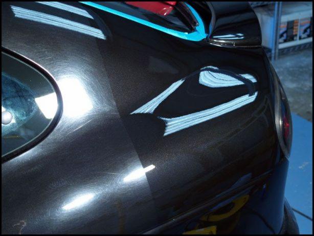 Błyszcząca, ciemna karoseria samochodu z widocznymi śladami polerowania i odbijającym się światłem, ukazująca różnicę w wyglądzie lakieru przed i po zabiegu.