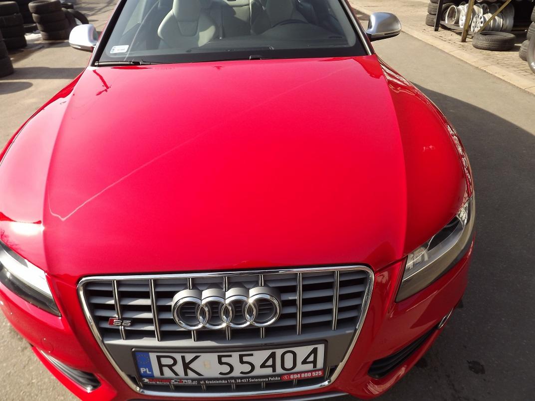 Błyszczący czerwony Audi S5 po polerowaniu lakieru, widoczne odbicie światła na masce, opony w tle.