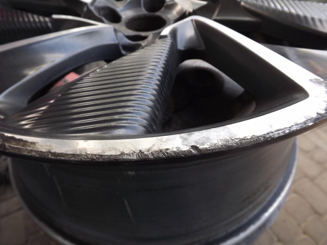 Uszkodzona felga aluminiowa z widocznymi śladami korozji i odpryskami lakieru na rancie, ukazana w zbliżeniu.