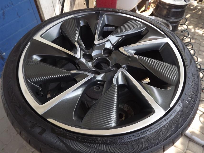 Felga samochodowa z oponą, pomalowana na szaro z elementami karbonowymi i srebrnym rantem, widoczne detale bieżnika opony i oznaczenia producenta Giugiaro.