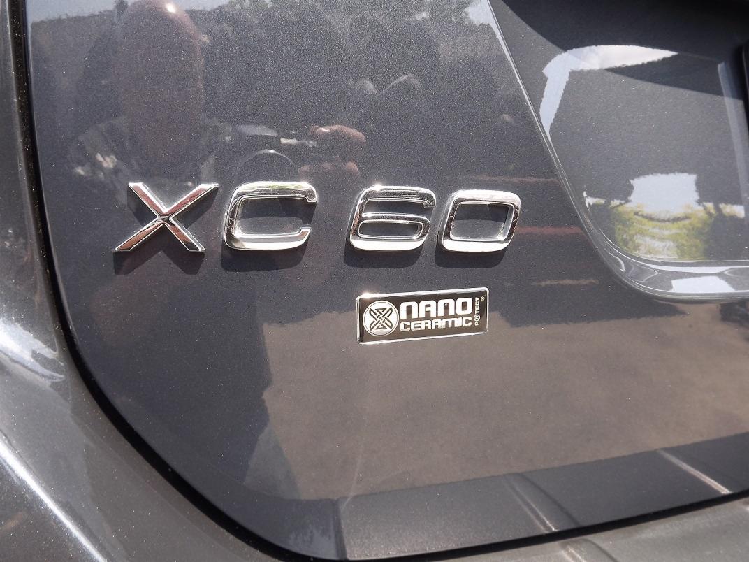 Szary samochód Volvo XC60 z emblematem Nano Ceramic Protect, widoczne odbicie otoczenia w lakierze.
