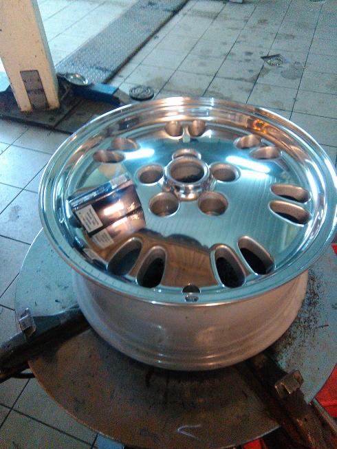 Błyszcząca, aluminiowa felga samochodowa na maszynie do montażu opon, z paczką papierosów leżącą wewnątrz, w warsztacie samochodowym.