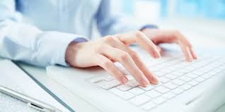 Dłonie kobiety piszącej na białej klawiaturze komputera, obok leży dokument i długopis, w tle jasne, rozmyte biuro.