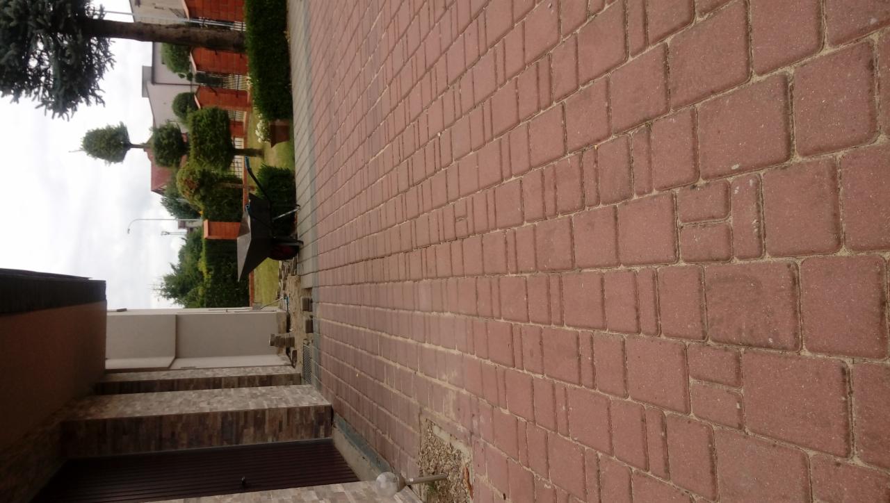 Ułożona czerwona kostka brukowa na podjeździe z widocznym fragmentem schodów wejściowych do domu oraz wózkiem budowlanym w tle.