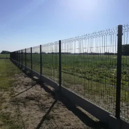 Długi, panelowy płot z podmurówką biegnący wzdłuż pola uprawnego, widok z zewnątrz posesji.