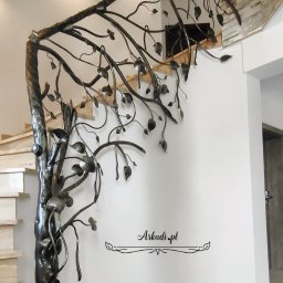 Arkadi - Kuta balustrada schodowa w kształcie drzewa z metalowymi liśćmi, zamontowana przy marmurowych schodach w jasnym wnętrzu z dekoracyjną ścianą z kamienia i logo firmy na ścianie.