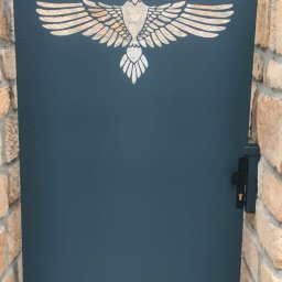Arkadi - Metalowa furtka wejściowa w kolorze grafitowym z wyciętym laserowo motywem orła, zamontowana między kamiennymi słupkami.