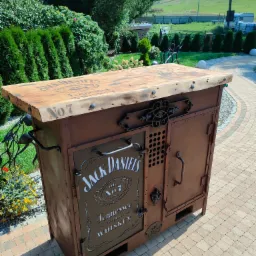 Rustykalna szafka barowa z metalu i drewna z motywem Jack Daniel's, umieszczona na brukowanym patio w ogrodzie.