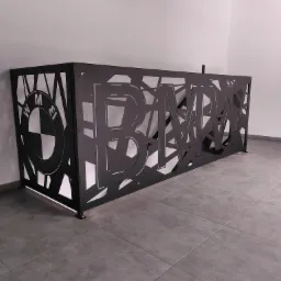 Czarna, metalowa konstrukcja z wyciętym logo BMW i abstrakcyjnymi wzorami, stojąca na szarych płytkach w minimalistycznym wnętrzu.