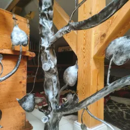 Metalowa balustrada wewnętrzna w kształcie drzewa z liśćmi, wsparta na drewnianej kolumnie w rustykalnym wnętrzu.