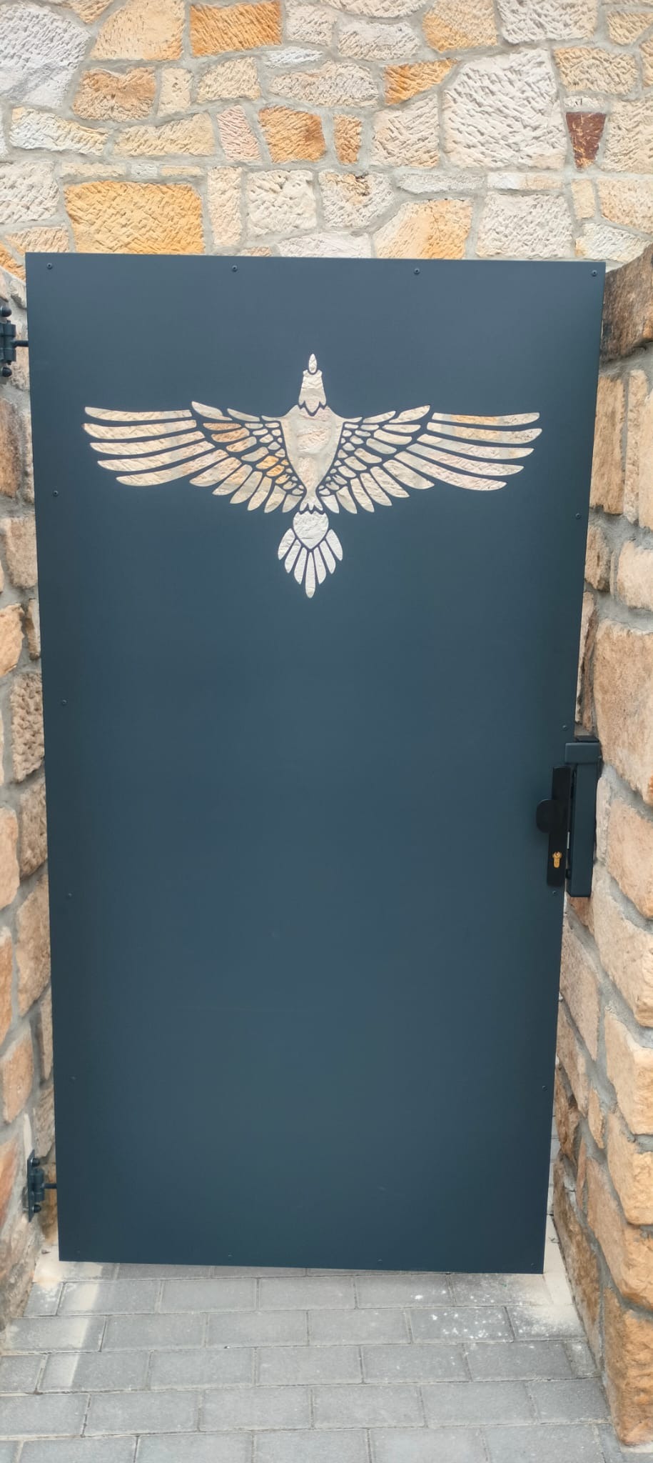 Metalowa furtka wejściowa w kolorze grafitowym z wyciętym laserowo motywem orła, zamontowana między kamiennymi słupkami.