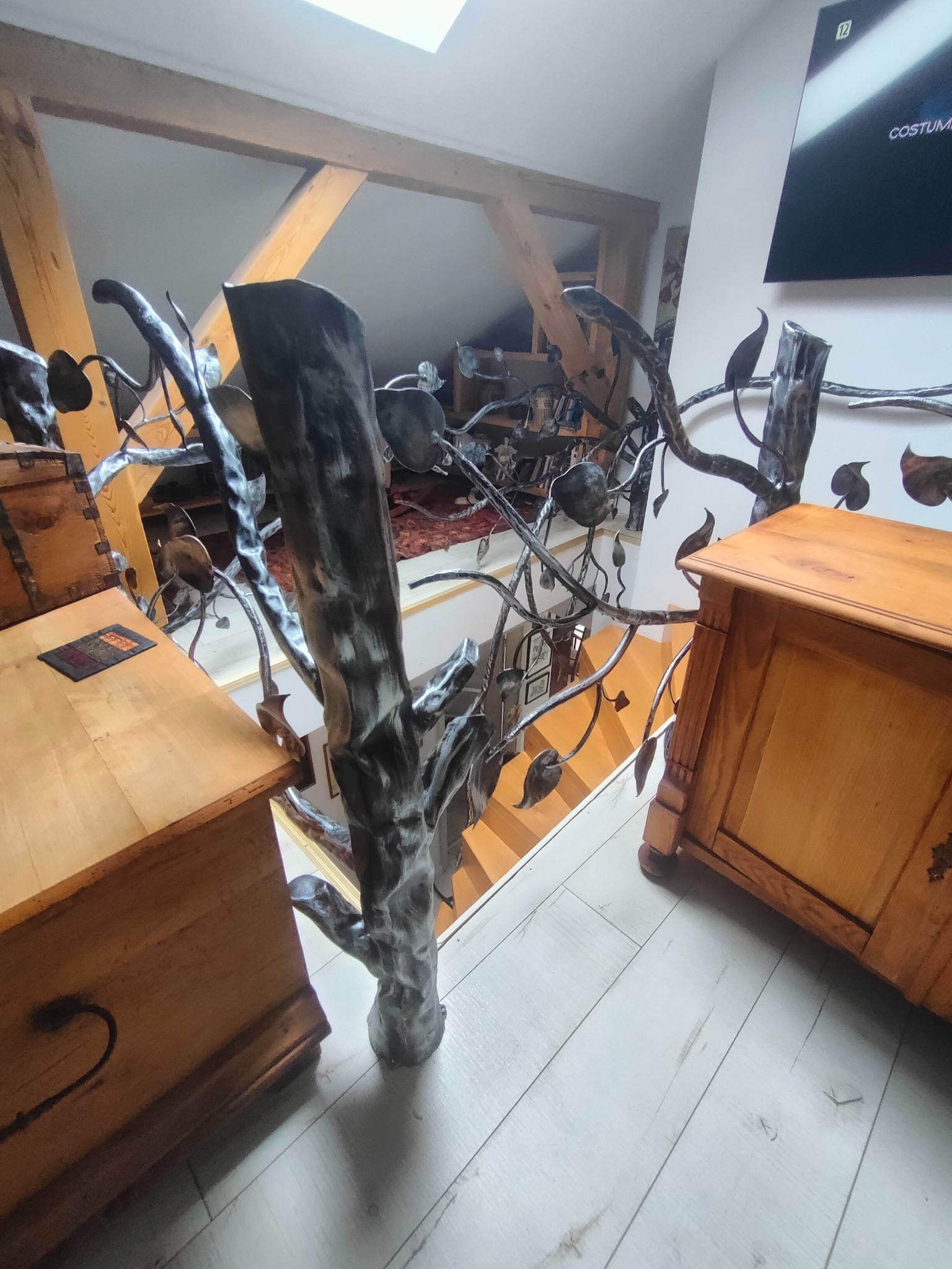 Metalowa balustrada o motywie drzewa z liśćmi, wykonana w Bolesławcu, zabezpieczająca schody i antresolę, widziana z góry, z elementami drewnianych skrzyń w kadrze.